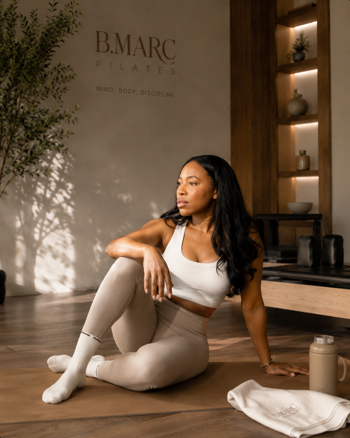 Founder seated on a mat with B.MARC water bottle and towel — calm studio practice